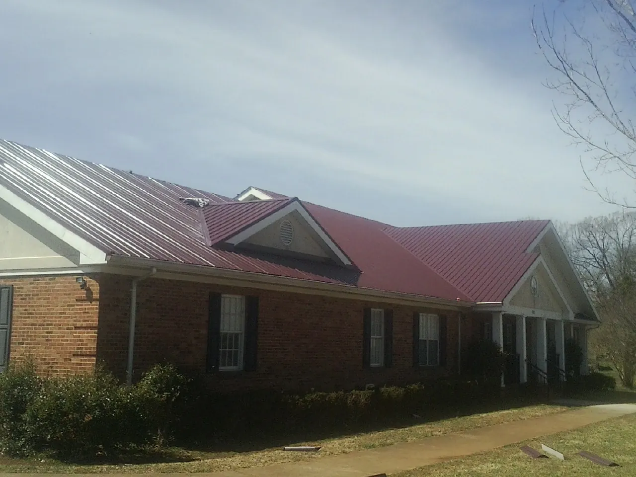 Red metal roof with gabled entries on a long brick building, from a Hail Damage Roof Repair job in Uniontown